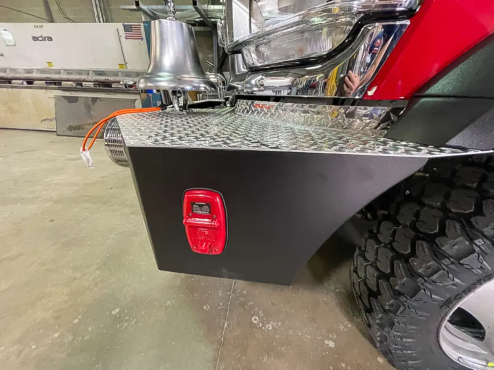 Exterior view of small fire truck showing cab, body compartments, and wheel/tire area.